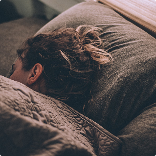 Person peacefully sleeping in bed, cozy gray bedding, restful sleep wellness concept